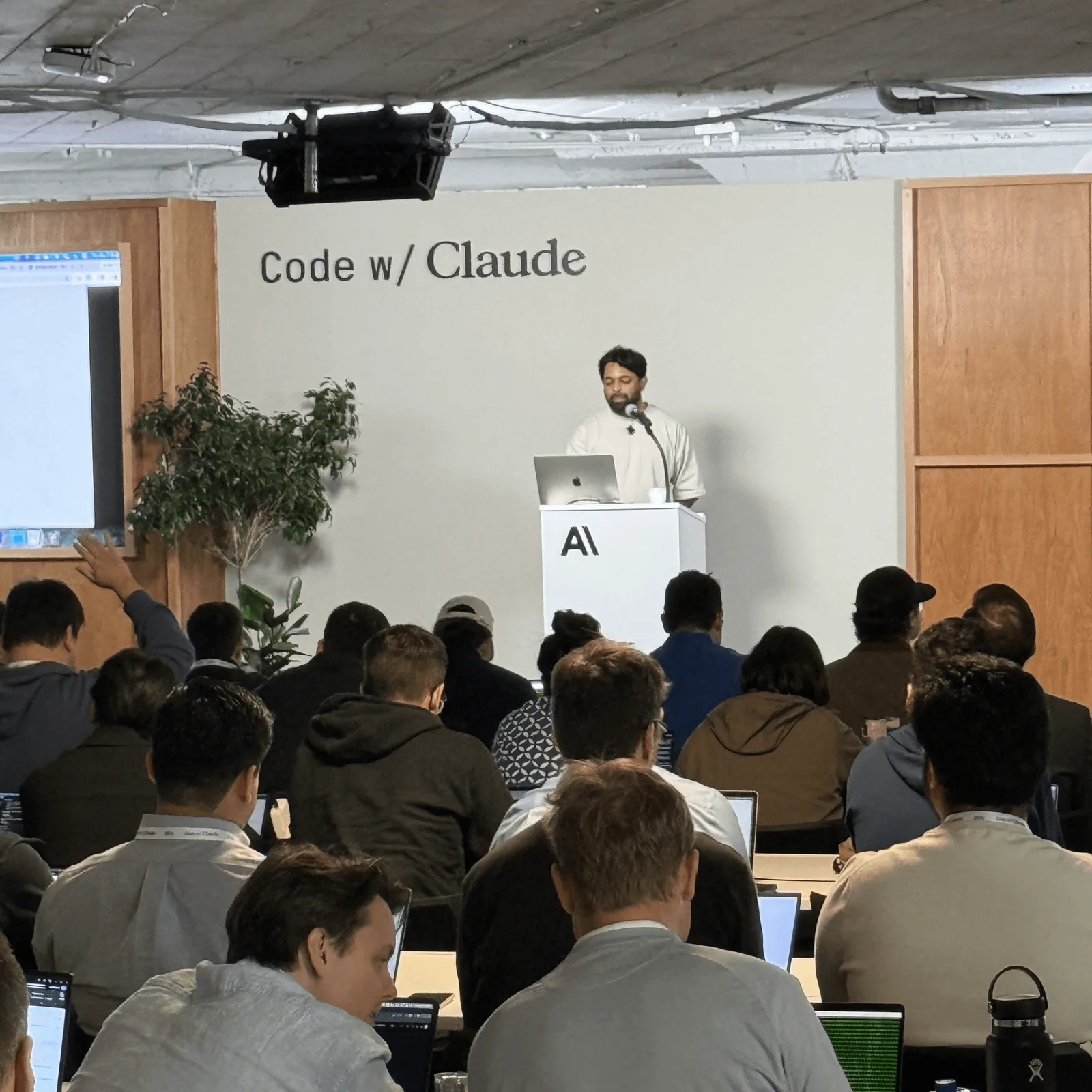 The workshop room, devs with laptops open, speaker at the Anthropic podium